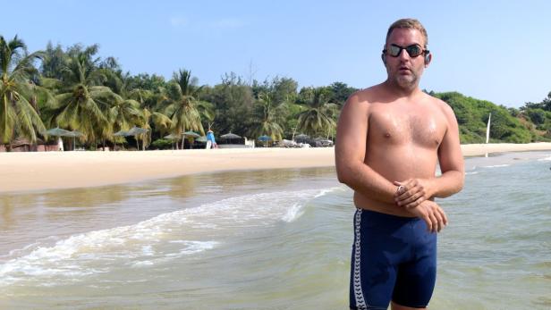 Ein Mann mit Schwimmbrille steht im Wasser an einem tropischen Strand.