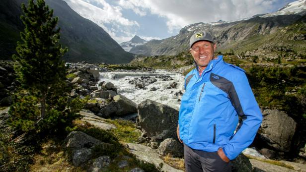 Ein Mann in Berglandschaft mit reißendem Fluss im Hintergrund.