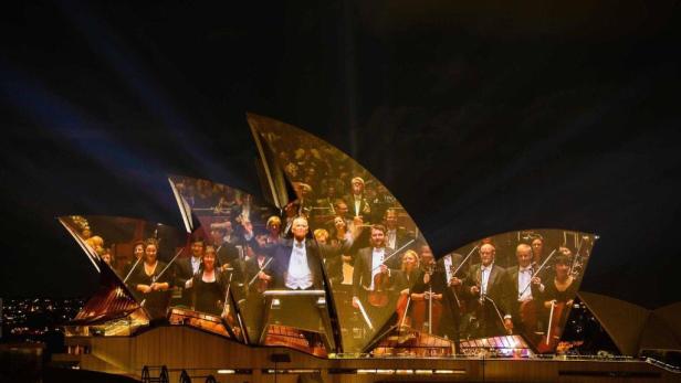 Das Opernhaus von Sydney ist nachts mit dem Bild eines Orchesters beleuchtet.