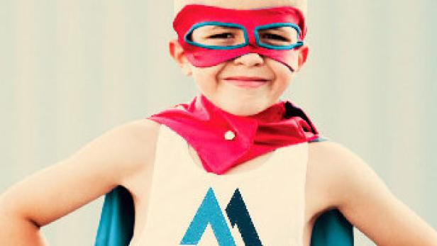 Ein lächelnder Junge verkleidet als Superheld mit roter Maske und Umhang.