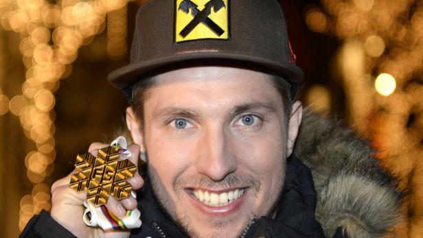 Ein Mann mit Mütze hält eine goldene Schneeflocken-Medaille in der Hand.