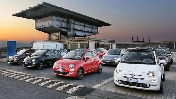 Mehrere Fiat 500 in verschiedenen Farben stehen vor einem modernen Gebäude.