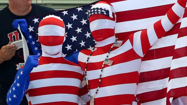Zwei Personen in Ganzkörperanzügen mit US-Flaggenmuster posieren vor einer US-Flagge.