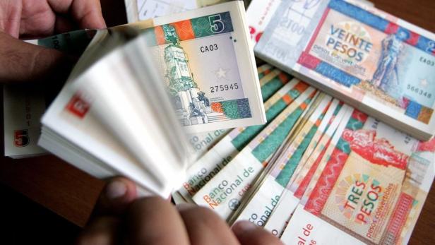 Hände blättern durch einen Stapel kubanischer Pesos verschiedener Nennwerte.