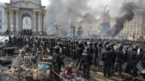 Eine Reihe von Polizisten steht vor Trümmern und Rauch auf einem Platz.