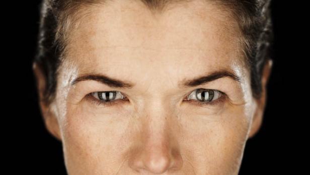 Porträt einer Frau mit ernstem Gesichtsausdruck vor schwarzem Hintergrund.