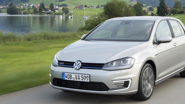 Ein silberner VW Golf fährt auf einer Landstraße an einem See entlang.