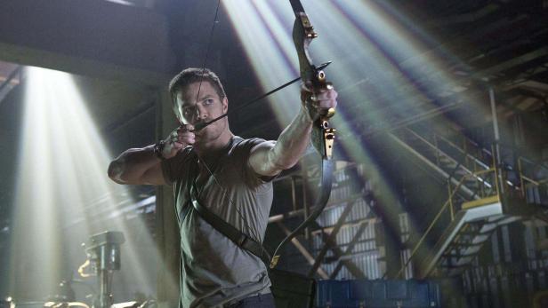 Ein Mann zielt mit Pfeil und Bogen in einer Lagerhalle.