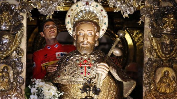 Ein Radrennfahrer steht hinter einer reich verzierten Heiligenfigur in einer Kirche.