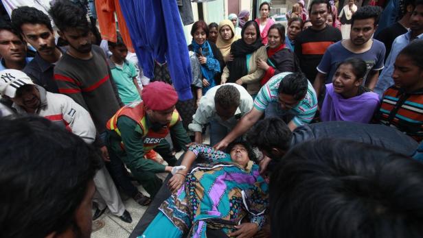 Rettungskräfte kümmern sich um eine bewusstlose Frau inmitten einer besorgten Menschenmenge.