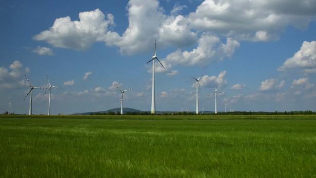 Windräder stehen auf einem grünen Feld unter einem bewölkten Himmel.