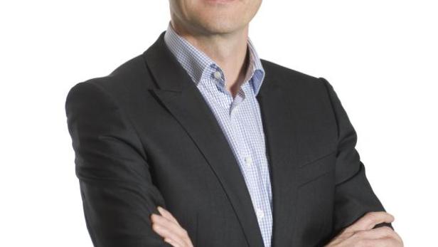 Ein Mann im Anzug mit verschränkten Armen vor einem weißen Hintergrund.