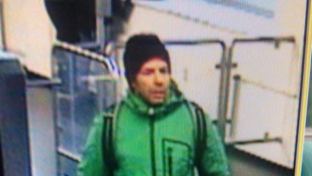 Ein Mann mit Mütze und grünem Anorak steht vor einem Gebäude.