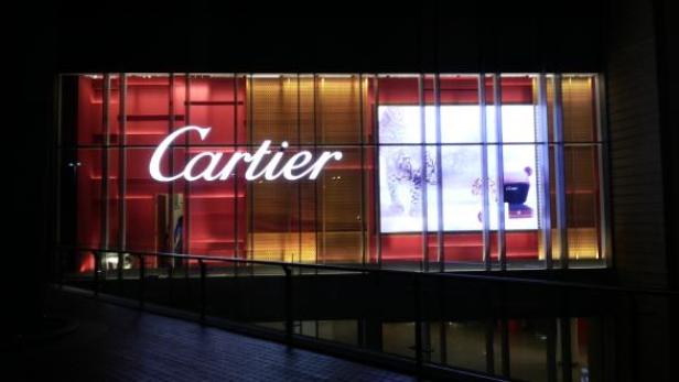 Ein Cartier-Geschäft mit einem beleuchteten Logo und einer Werbeanzeige im Fenster.