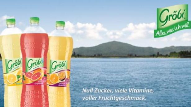 Drei Flaschen Gröbi-Limonade stehen vor einem See mit Bergen im Hintergrund.