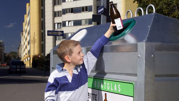 Ein Junge wirft eine Glasflasche in einen Container für Buntglas.