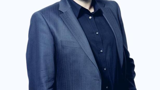 Ein Mann mit Brille, Anzug und schwarzem Hemd lächelt in die Kamera.