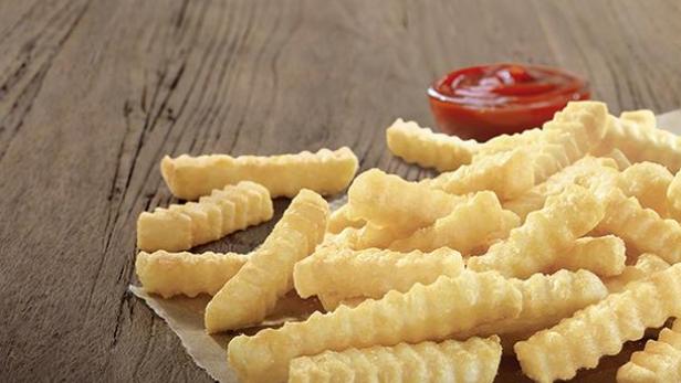 Eine Portion gewellte Pommes Frites mit einem Schälchen Ketchup auf einem Holztisch.