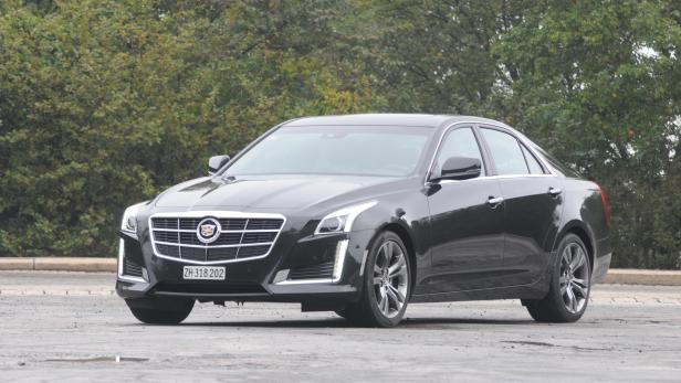 Ein schwarzer Cadillac CTS steht vor einer grünen Baumreihe.