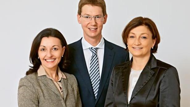 Drei Personen in formeller Kleidung lächeln in die Kamera.