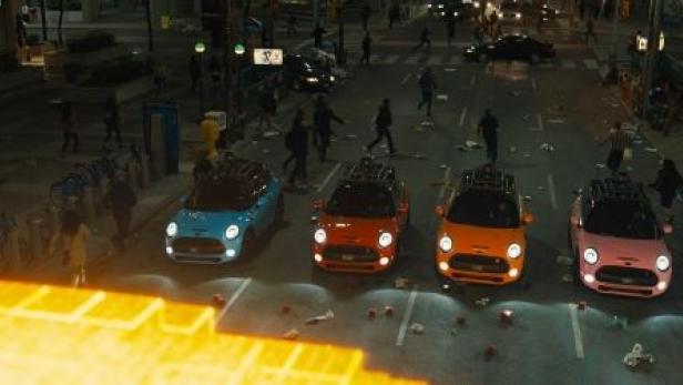 Vier farbige Minis stehen auf einer belebten Straße bei Nacht.