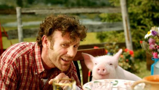 Ein Mann sitzt mit einem kleinen Schwein an einem Tisch im Freien.