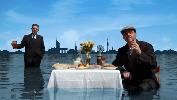 Zwei Männer sitzen an einem gedeckten Tisch im Wasser, im Hintergrund die Skyline von Wien.