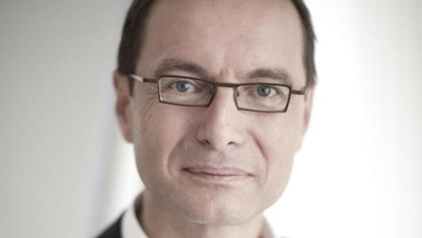 Ein Mann mit Brille und dunklem Anzug blickt in die Kamera.