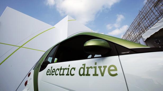 Ein weißer Smart mit grünem Akzent und dem Schriftzug „electric drive“ vor einem weißen Gebäude.