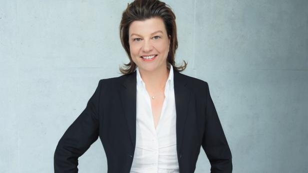 Eine Frau in Blazer und Bluse lächelt in die Kamera.