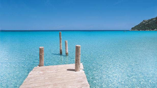 Ein Holzsteg führt in das türkisfarbene, klare Wasser eines tropischen Strandes.
