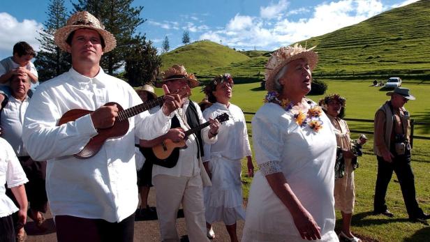 Eine Gruppe von Menschen in traditioneller Kleidung spielt Ukulele und singt im Freien.