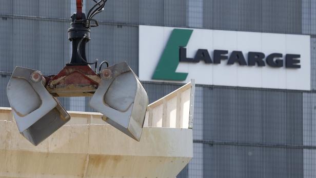 Ein Greifbagger hebt eine Betonladung vor dem Hintergrund des Lafarge-Logos.