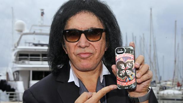 Gene Simmons präsentiert ein Handy mit einem „Kiss“-Motiv vor einem Yachthafen.
