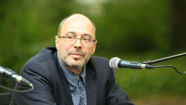 Ein Mann mit Brille sitzt vor Mikrofonen.