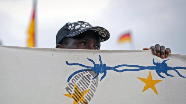 Ein Mann hält ein Banner mit Stacheldraht und Sternen vor einer Deutschlandflagge.