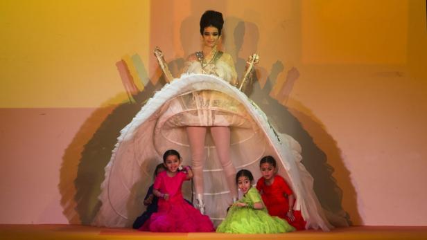 Eine Frau in einem extravaganten Kleid mit mehreren Kindern auf einer Bühne.