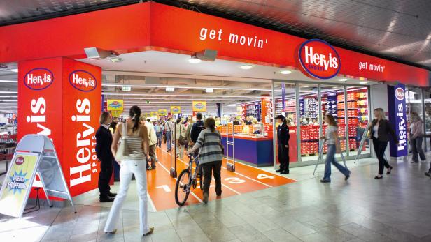 Kunden betreten ein Hervis Sportgeschäft mit roter Laufbahn am Eingang.