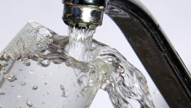 Ein Glas wird mit Wasser aus einem Wasserhahn gefüllt.