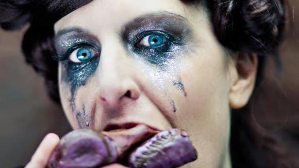 Eine Frau mit starkem Make-up isst eine lila Süßigkeit.