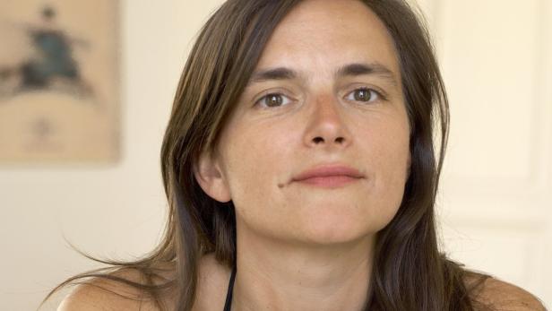 Porträt einer Frau mit braunen Haaren und einem Muttermal auf der Wange.