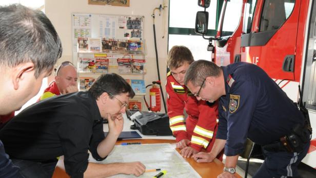 Feuerwehrleute und ein Polizist beugen sich über eine Karte in einer Feuerwache.