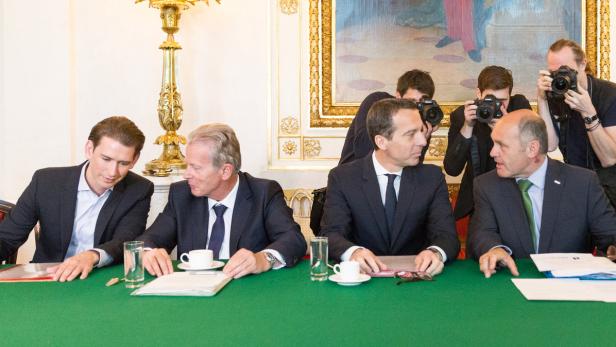 Mehrere Männer in Anzügen sitzen an einem Tisch, während Fotografen Fotos machen.