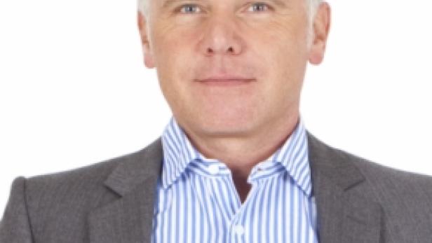 Ein Mann mit blonden Haaren und einem grauen Sakko vor einem weißen Hintergrund.