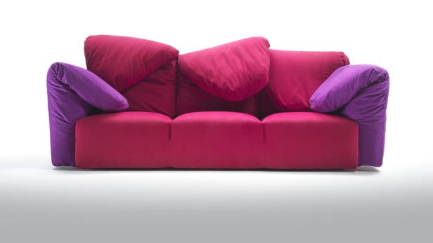 Ein dreisitziges Sofa mit pinkfarbenen Kissen und lila Armlehnen vor einem weißen Hintergrund.