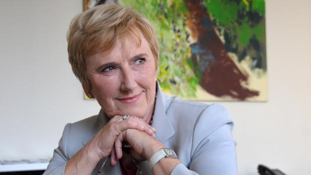 Eine Frau in einem hellgrauen Blazer lächelt und blickt nach links.