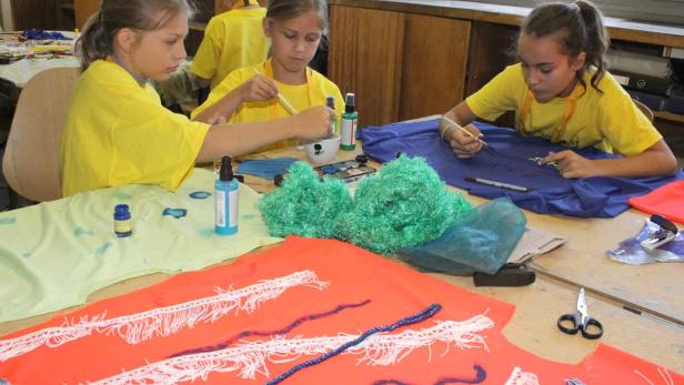 Drei Mädchen bemalen Stoffe in verschiedenen Farben mit Pinseln.