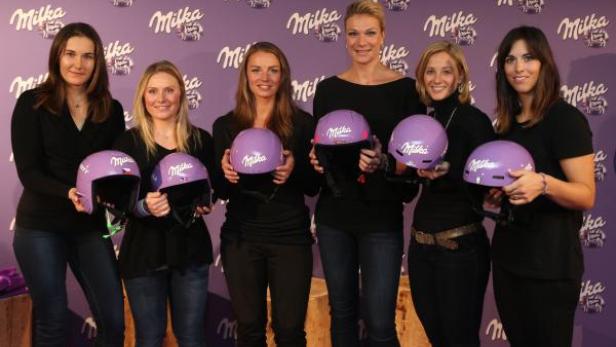 Sechs Frauen posieren mit lila Skihelmen der Marke Milka vor einem lila Hintergrund mit Milka-Logo.