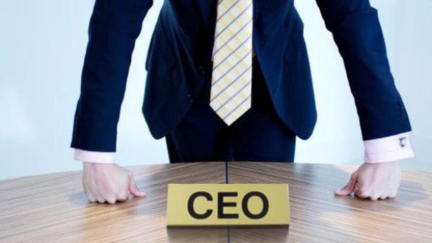 Ein Mann in Anzug steht mit geballten Fäusten an einem Tisch mit einem Schild „CEO“.
