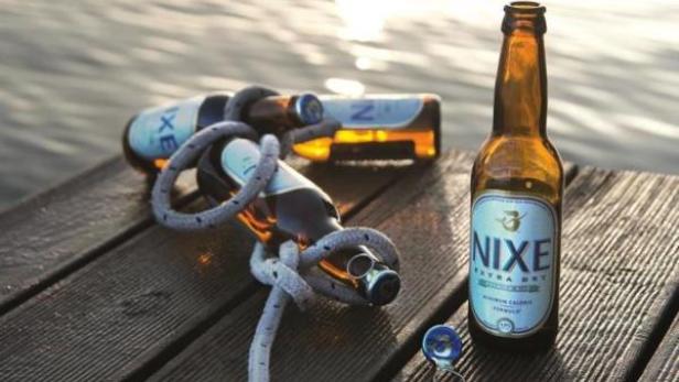 Zwei Flaschen Nixe Bier, von denen eine mit einem Seil umwickelt ist, liegen auf einem Holzsteg.